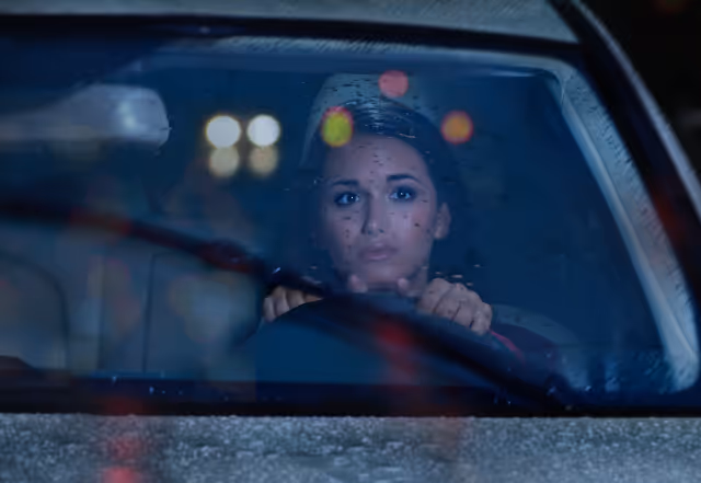 A girl driving a car at night with bokeh of car light reflections on her window