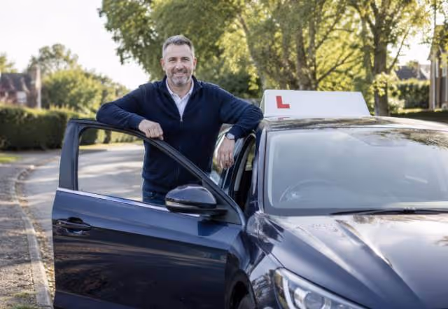 A driving instructor standing beside a learner car after a lesson