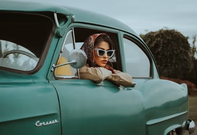 A young woman wearing sunglasses looking out of the window of a classic car